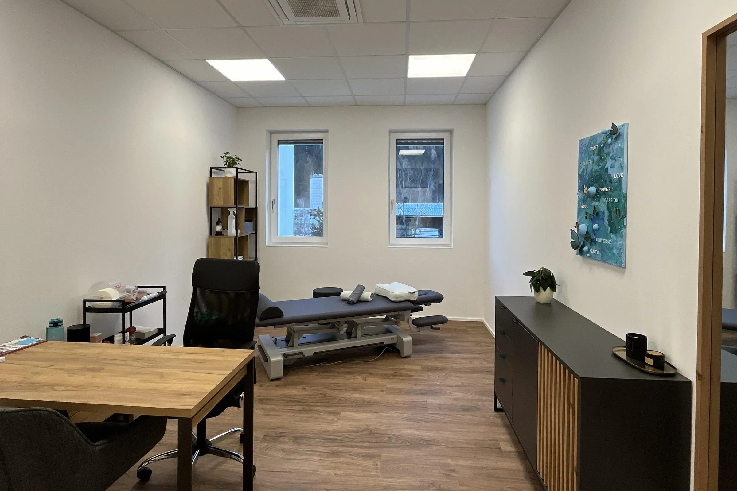 Behandlungsraum in Imst mit Therapieliege, Schreibtisch und zwei Fenstern