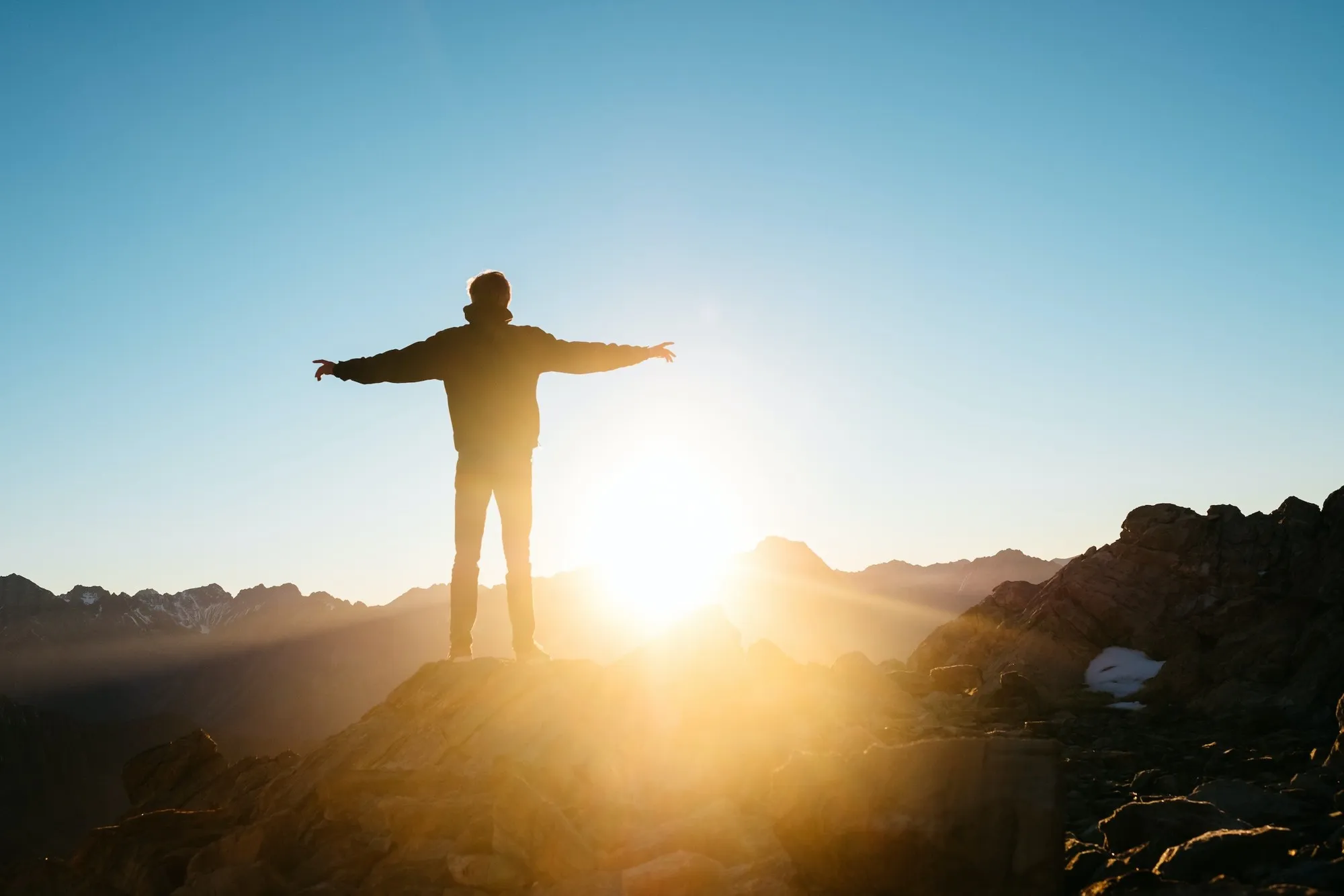 Person mit ausgebreiteten Armen auf einem Berggipfel bei Sonnenaufgang