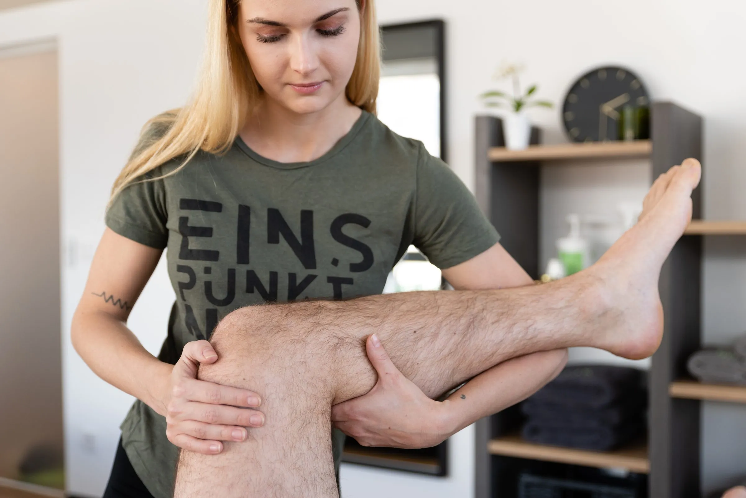 Physiotherapeutin mobilisiert das Knie eines Patienten auf der Behandlungsliege