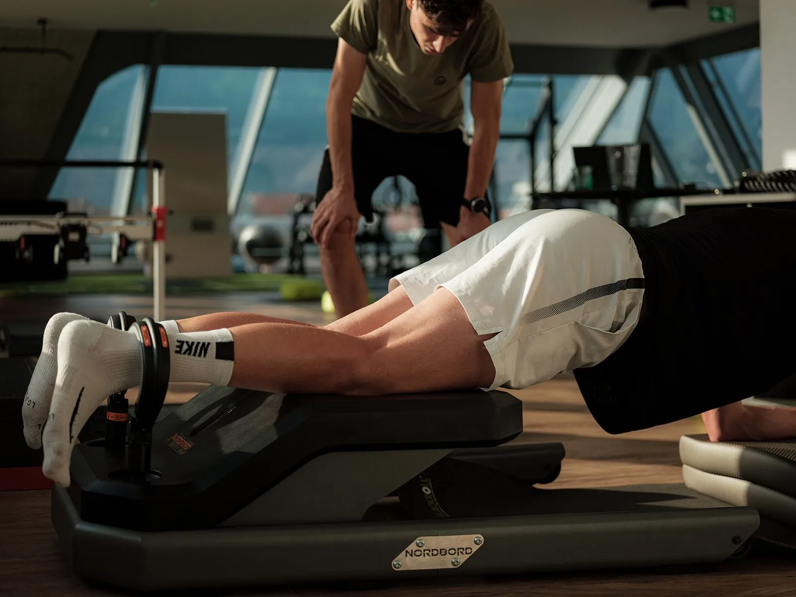 Sportler bei der Nordic-Hamstring-Kraftmessung, ein Sportwissenschafter sichert ab
