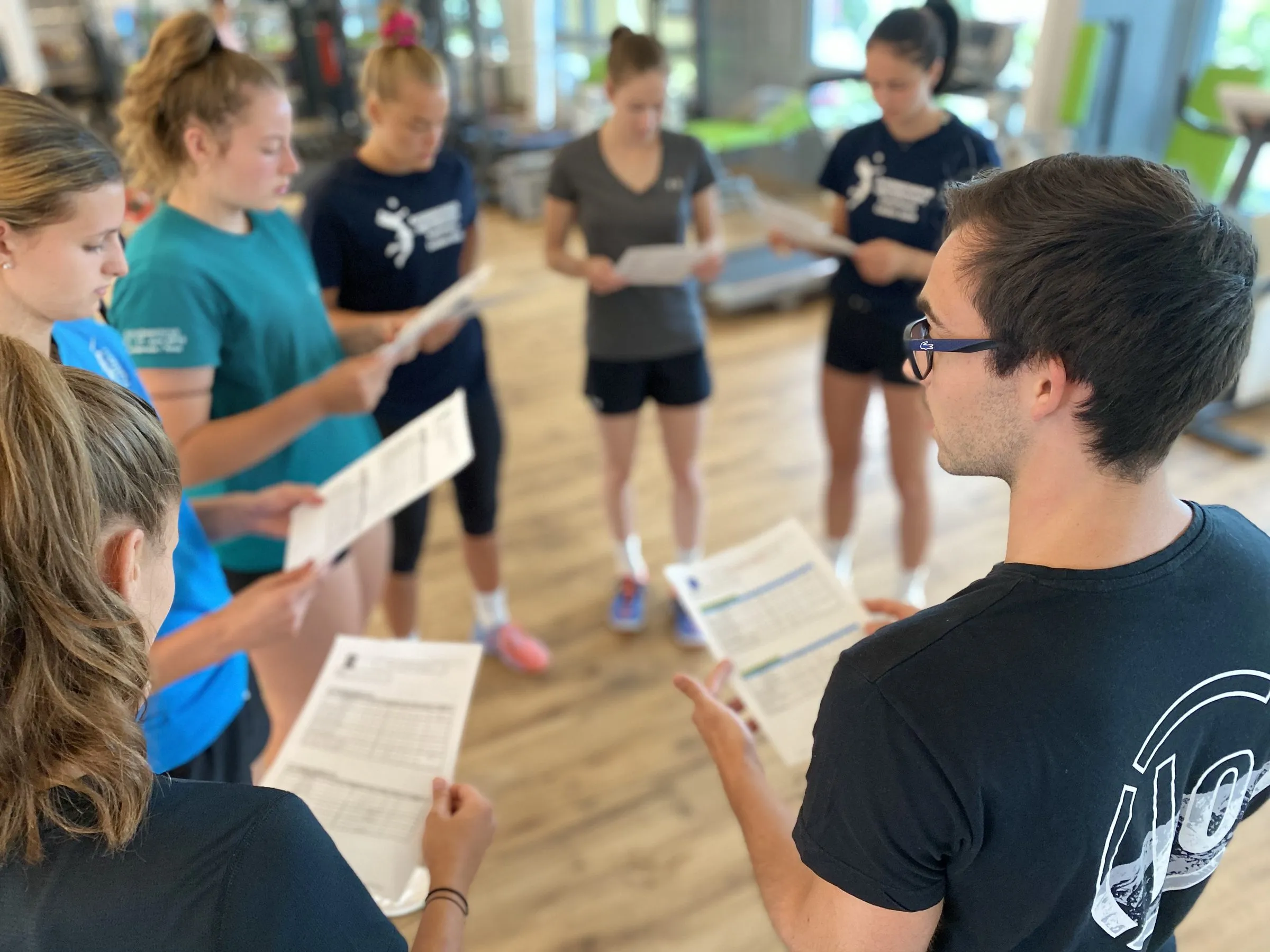 Athletinnen und Athleten mit Unterlagen bei einem Workshop mit einem Trainer